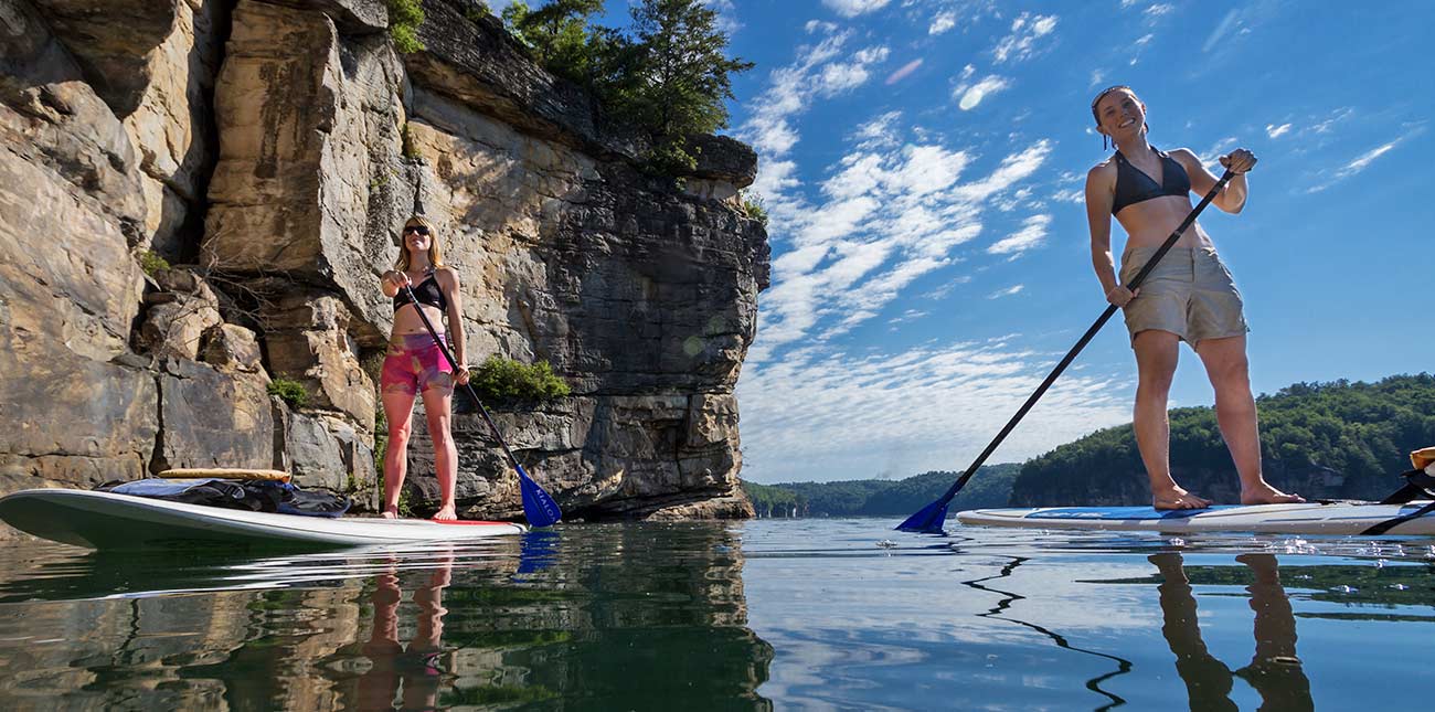 Two friends paddle across the water under a cliff line at Summersville Lake on the pontoon adventure trip. 