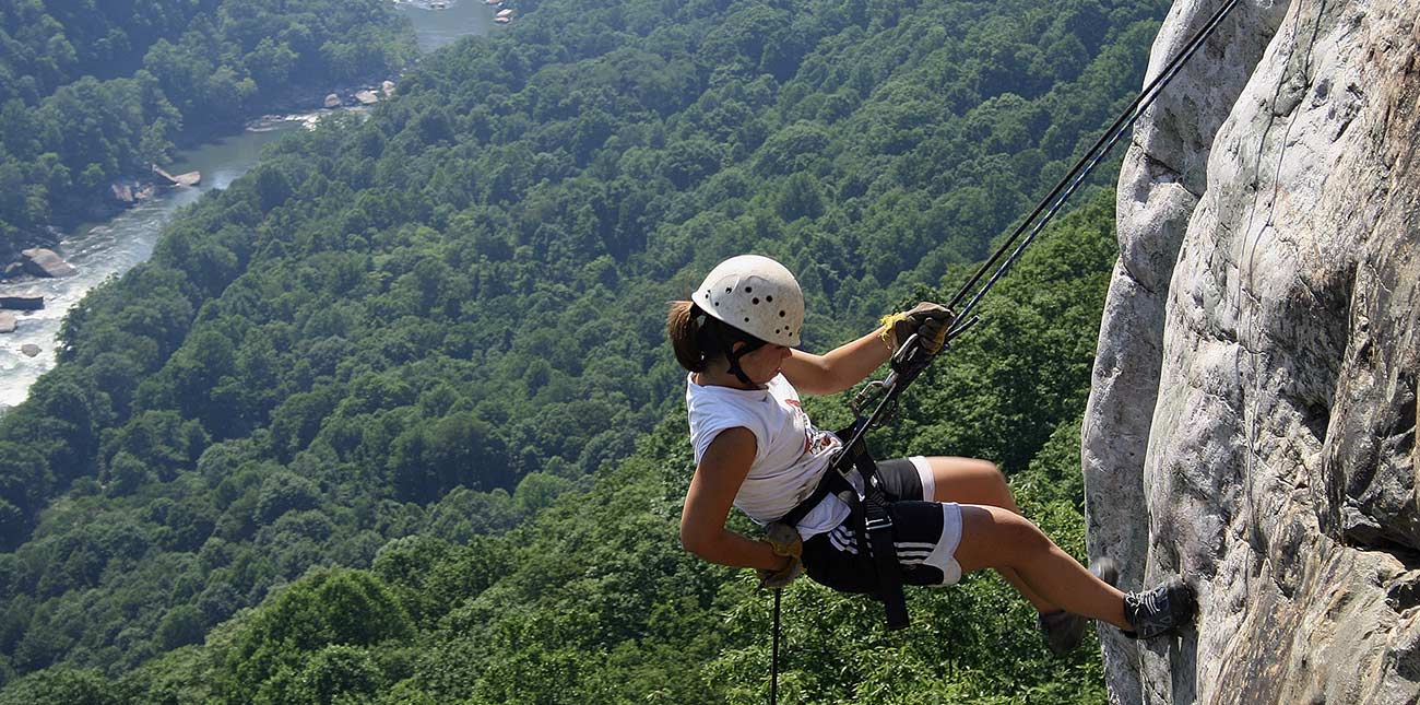 A woman rappels down the rock face of the lower New River Gorge.
